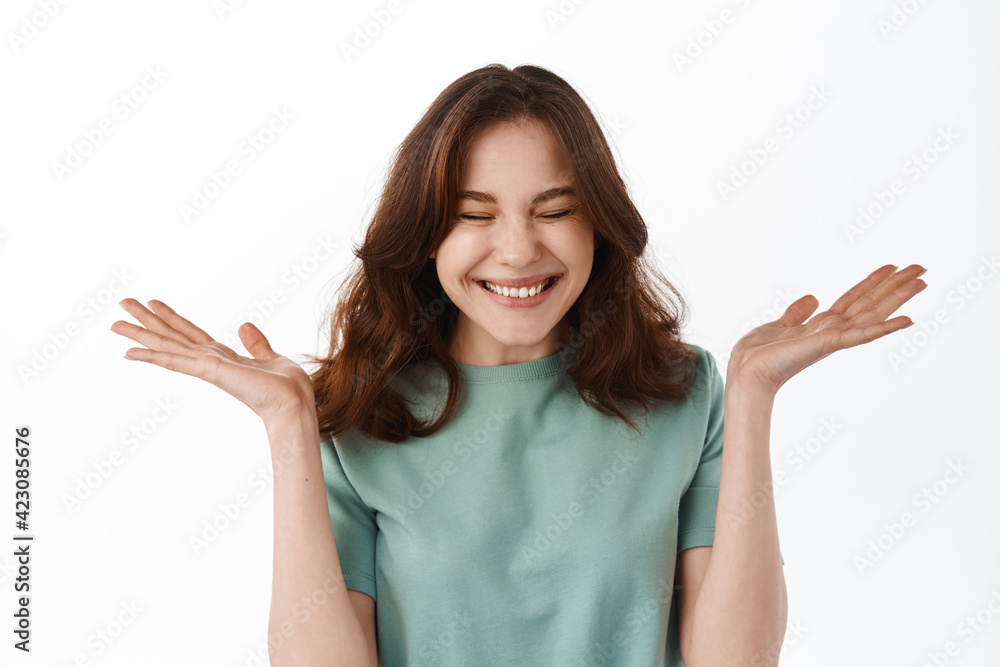 Close up of woman rejoicing and feeling super happy, got lucky, raising hands up and close eyes while smiling excited, standing against white background Close up of woman rejoicing and feeling super happy, got lucky, raising hands up and close eyes while smiling excited, standing against white background