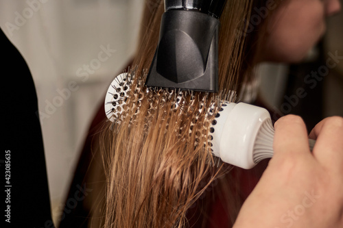 The hairdresser hands dry the hair with an electric hair dryer and a circular comb. Taking care of your hair. Beauty salon.