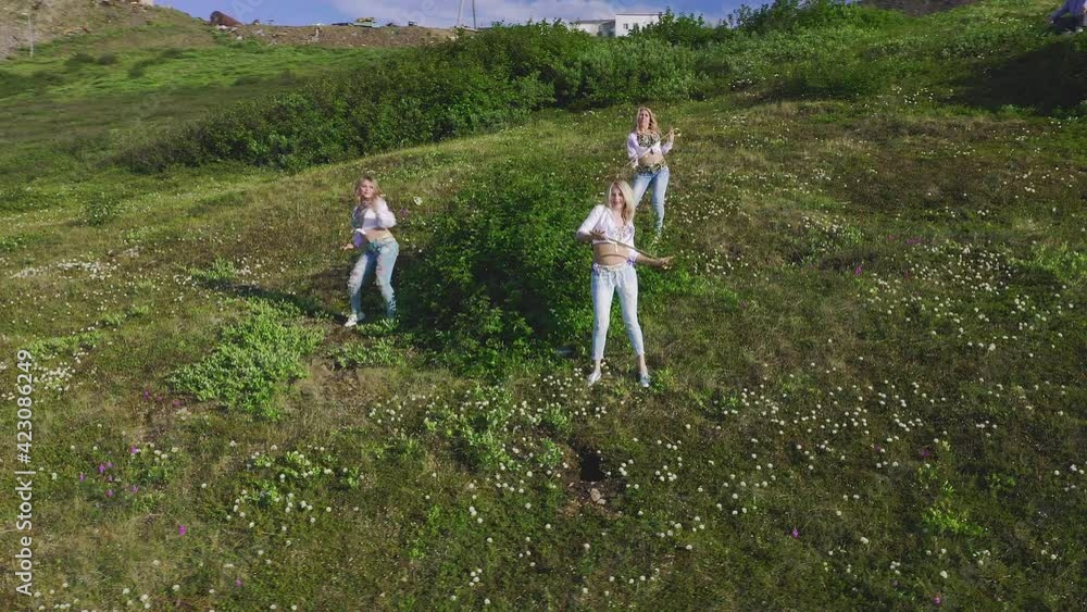 Aerial view from drone flying over of a three of European women in exotic costumes dancing oriental dances with a cane on the background of the green tundra and water, in summer. Aerial view from drone flying over of a three of European women in exotic costumes dancing oriental dances with a cane on the background of the green tundra and water, in summer.