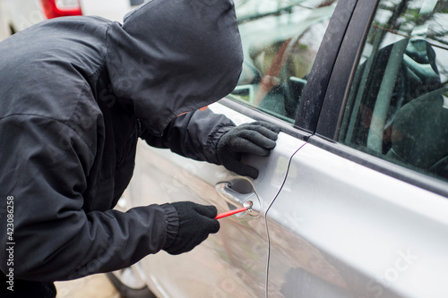 Robber man in black hoodie jacket using a screwdriver to break lock and steal a vehicle. Car thief or theft for insurance concept
