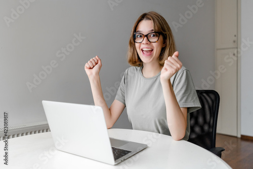 young happy woman smiling sitting with laptop in the apartment won the prize