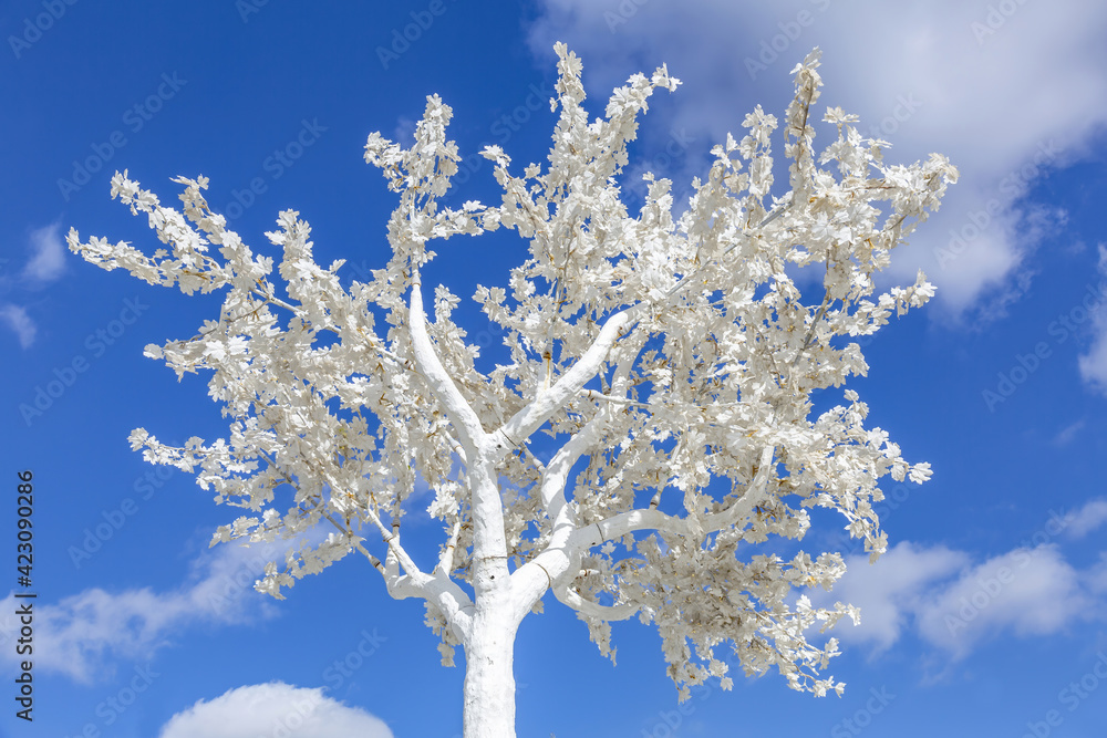 Unusual branches of a white decorative plastic tree against a bright blue cloudy sky