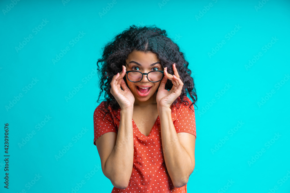Dark skinned girl in trendy spectacles is looking directly to the camera her eyes wide open and rounded mouth in surprisement, amazement Dark skinned girl in trendy spectacles is looking directly to the camera her eyes wide open and rounded mouth in surprisement, amazement