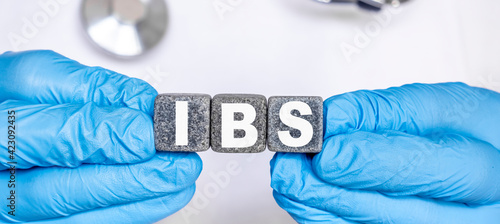 IBS Irritable bowel syndrome - word from stone blocks with letters holding by a doctor's hands in medical protective gloves
