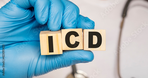 ICD Implantable cardioverter defibrillator - word from wooden blocks with letters holding by a doctor's hands in medical protective gloves. Medical concept.