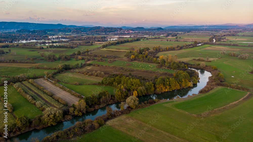 Spectacular aerial panorama of river flowing through fields at sunset.