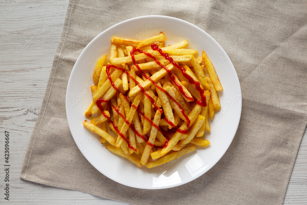 Homemade French Fries with Ketchup, Salt and Pepper on a white plate on a white wooden table, top view. Flat lay, overhead, from above. Homemade French Fries with Ketchup, Salt and Pepper on a white plate on a white wooden table, top view. Flat lay, overhead, from above.