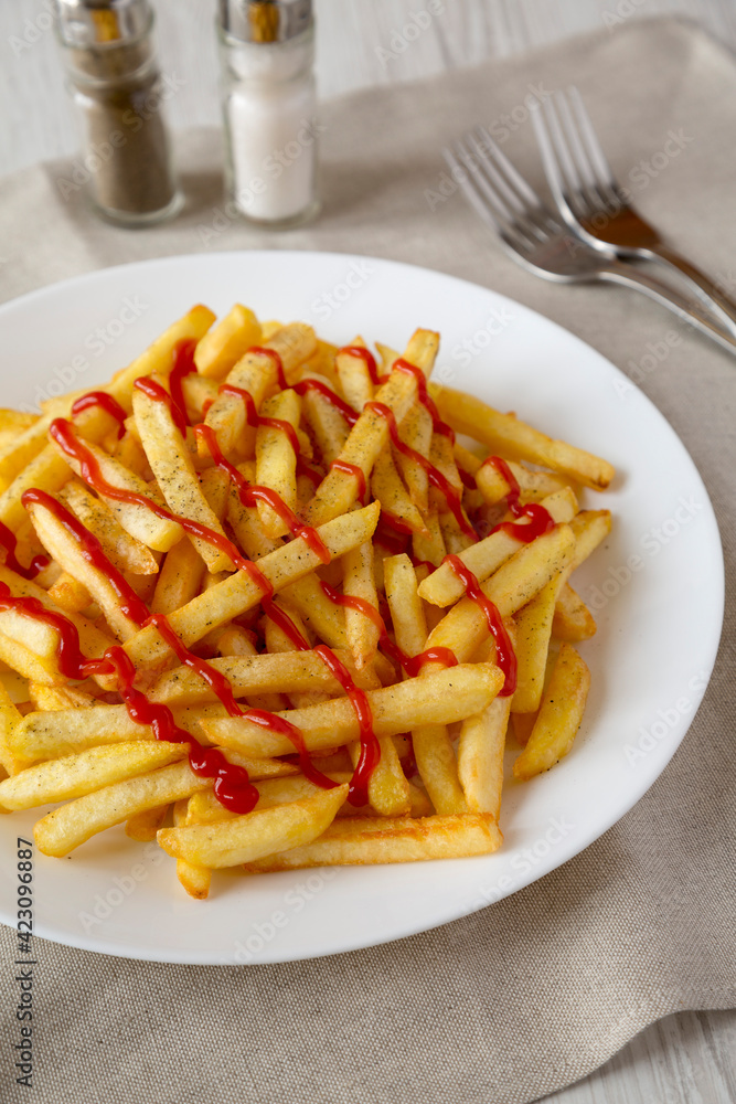 Homemade French Fries with Ketchup, Salt and Pepper on a white plate on a white wooden background, side view. Close-up. Homemade French Fries with Ketchup, Salt and Pepper on a white plate on a white wooden background, side view. Close-up.