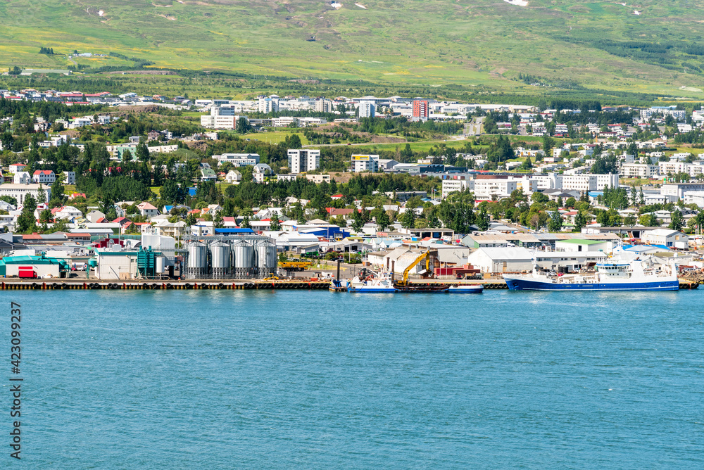 Harbour and an industrial park along a fjord  on a sunny spring day. Hillside residential buildings are in background. Akureyri, Iceland.