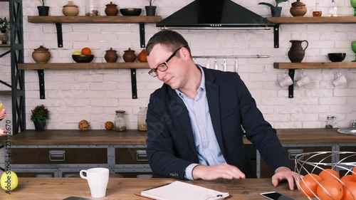 Cheerful smiling entrepreneur in a jacket and glasses juggles three lemons, drops them and waves his hand in frustration while sitting at home in the kitchen, slow motion