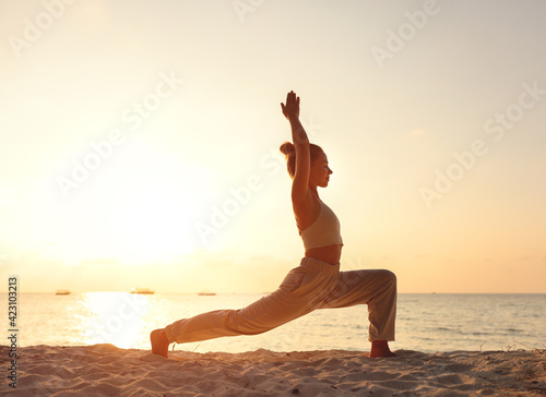 Female practicing Crescent Lunge pose on sunset beach