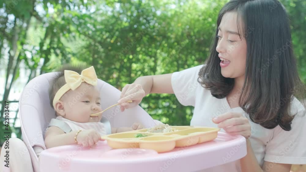 4k Mother feeding baby infant daughter toddler on highchair in a garden 4k Mother feeding baby infant daughter toddler on highchair in a garden
