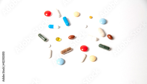 many pills of different shapes and different colors on a white background
