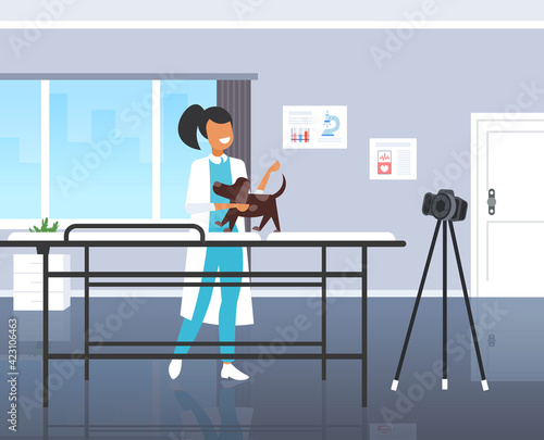 female veterinarian blogger checking dog at veterinarian clinic woman recording online video with camera on tripod blogging concept modern vet clinic interior horizontal full length