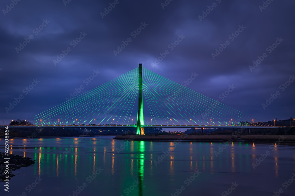 Modern line bridge illuminated with green lights for St. PAtricK in Waterford Ireland. Overnight.