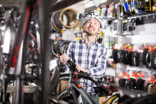 interested man in helmet chooses for himself sports bike in bicycle shop from a range