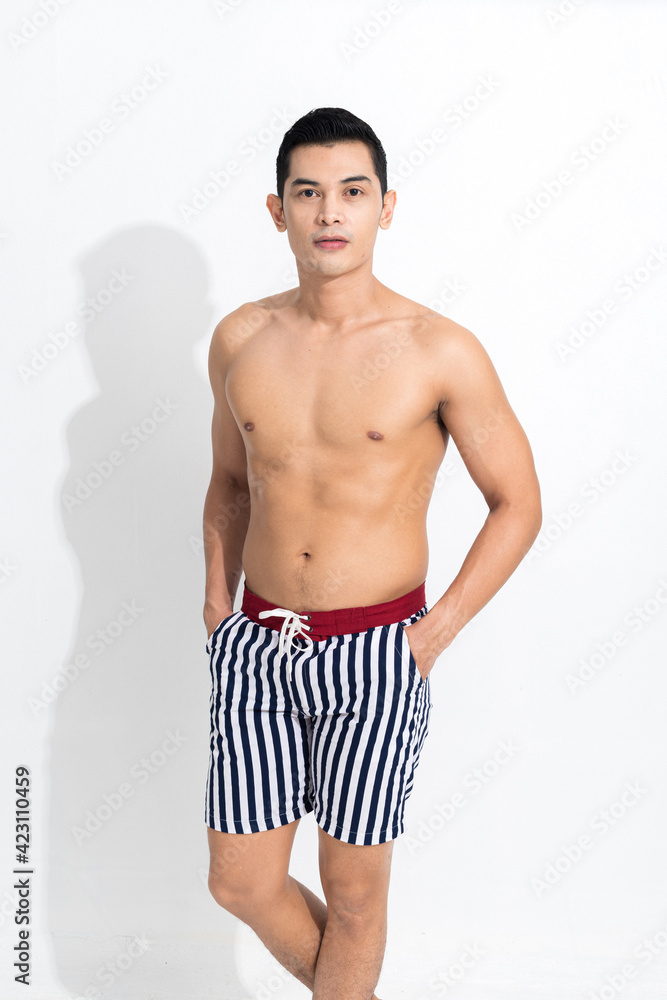 Young muscular guy in striped beach shorts sunbathing at studio shot isolated on white background. Fashion summer concept. Young muscular guy in striped beach shorts sunbathing at studio shot isolated on white background. Fashion summer concept.