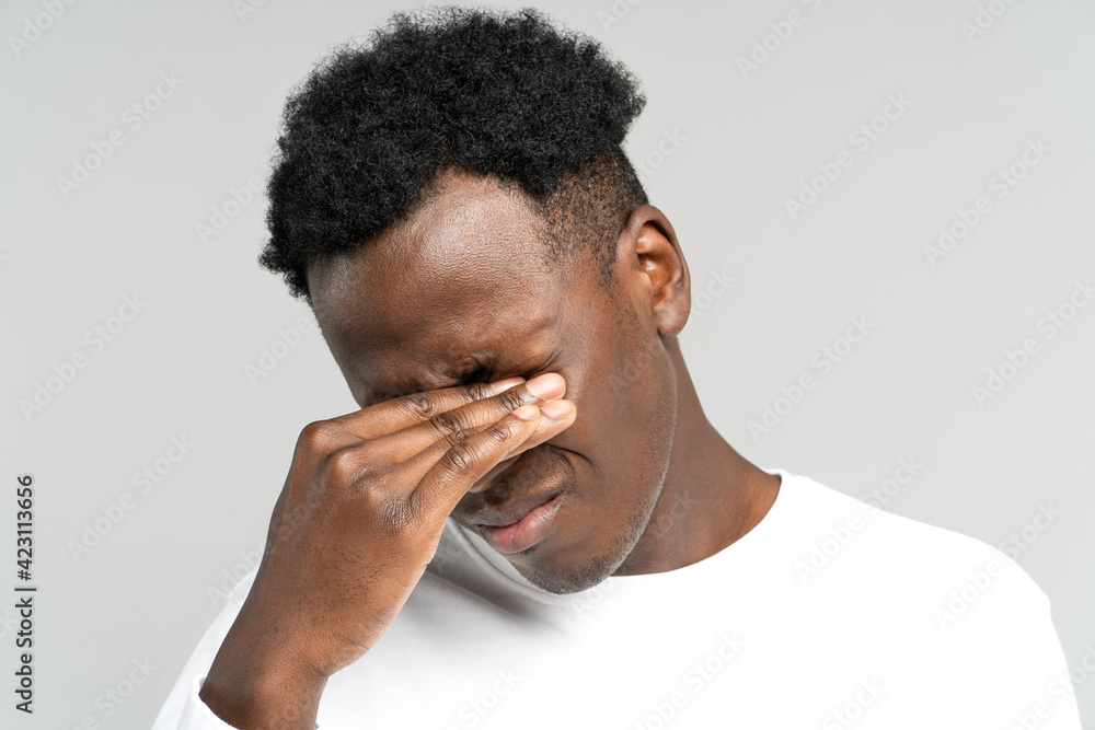 Sleepy African American man rubbing his eyes, feels tired after work on laptop computer, isolated on studio grey white background. Exhausted black male wants to sleep. Overwork, chronic fatigue eyes. Sleepy African American man rubbing his eyes, feels tired after work on laptop computer, isolated on studio grey white background. Exhausted black male wants to sleep. Overwork, chronic fatigue eyes.