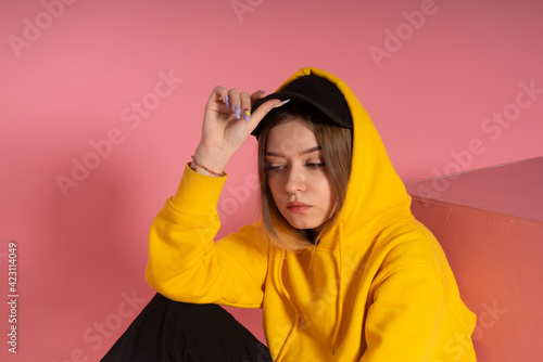 LGBTQ woman in a yellow hoodie sits on pink background © vkfoto