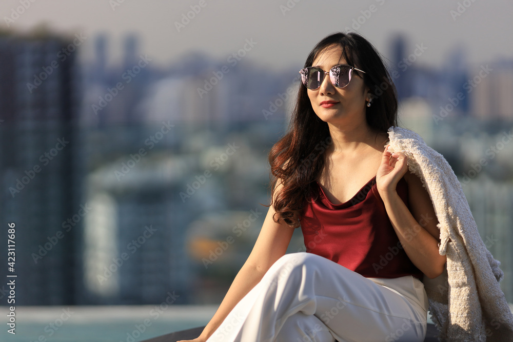 Luxury Asian CEO woman entrepreneur sitting on the rooftop looking to the sun with skyscraper and cityscape on the background with copy space