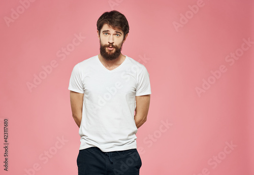 A guy with a beard on a pink background, a white T-shirt and dark trousers