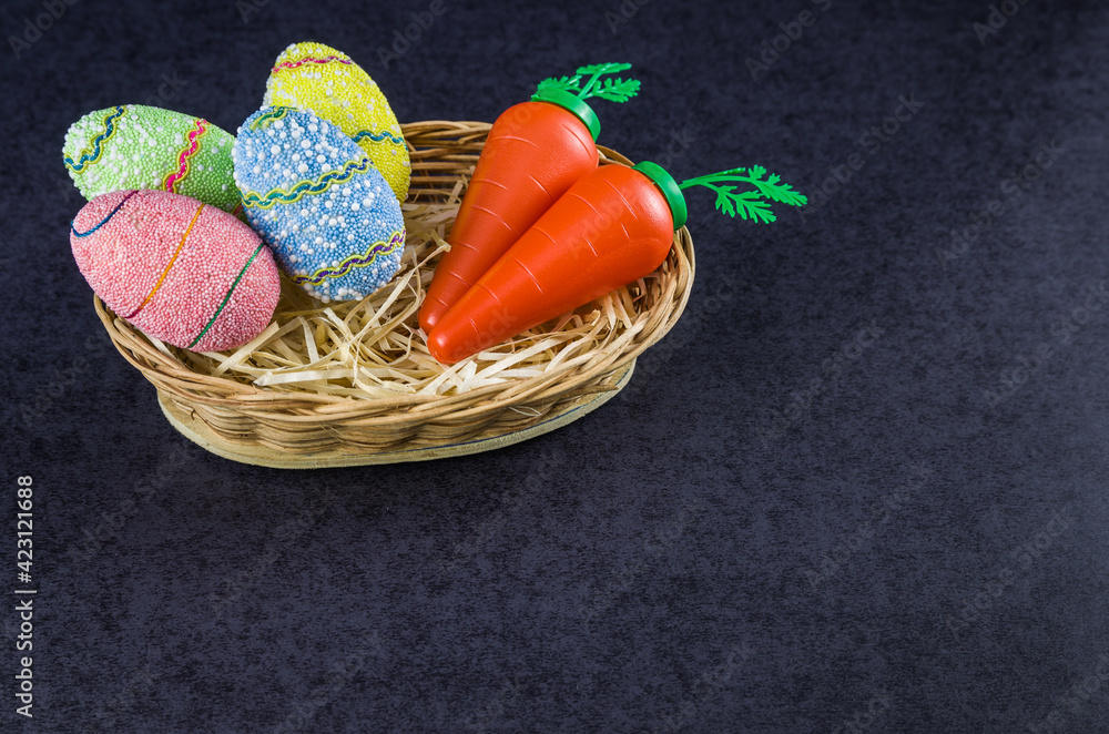 Easter colored eggs and carrots in a basket isolated on a trendy black background.
