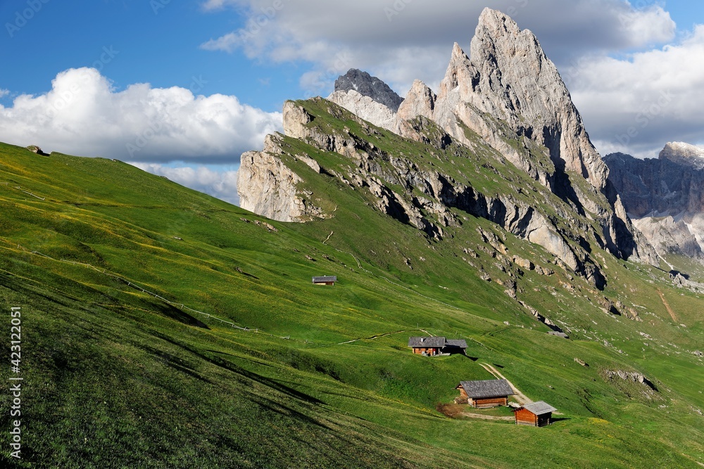 Beautiful scenery of Dolomites on a sunny summer day with view of majestic Odle (Geisler) mountain peaks in background & wooden huts on grassy hills at Seceda, Val Gardena, South Tyrol, Italy, Europe