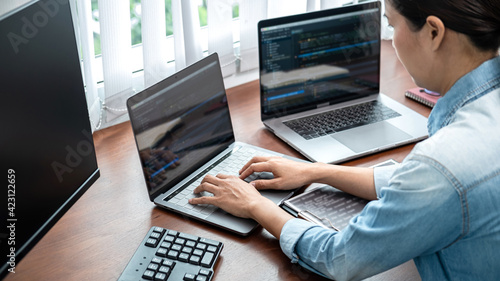 Asian programmer woman looking on multiple computer screen to typing coding database and development website