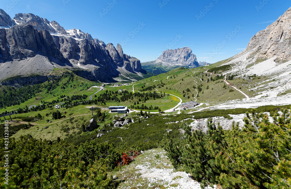 Scenery of Gardena Pass on a sunny summer day with rugged Sella & Sassolungo mountains in background, highways & hiking trails winding through the green grassy valley in Dolomites, South Tyrol, Italy