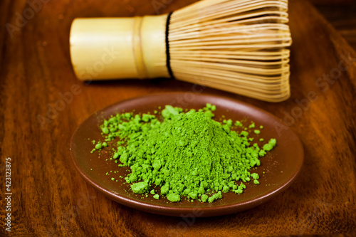 Green powdered matcha tea in a plate and bamboo matcha tea whisk also know as chasen on a wooden background.