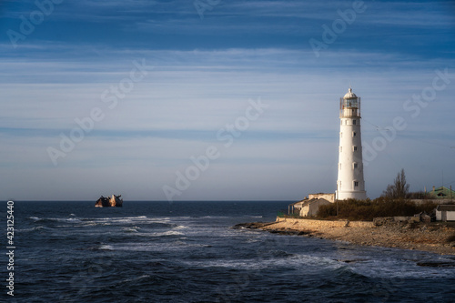 Lone beacon guards the ships. The lighthouse shows the way for boats. Wrecked ship lays nearby