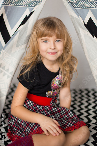 little blonde girl in socks, a skirt and a T-shirt sits in a tent