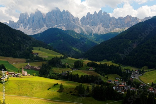 Idyllic scenery of Val di Funes on a cloudy summer day with rugged peaks of Odle mountain in background & a church in Village Santa Maddalena in the green grassy valley in Dolomiti, South Tyrol, Italy