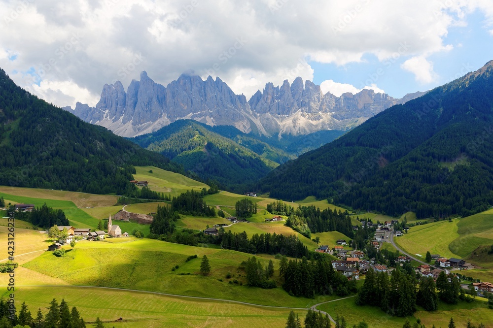 Summer scenery of idyllic Val di Funes with rugged peaks of Odle (Geisler) mountain range in background & a church in Village Santa Maddalena in the green grassy valley in Dolomiti, South Tyrol, Italy