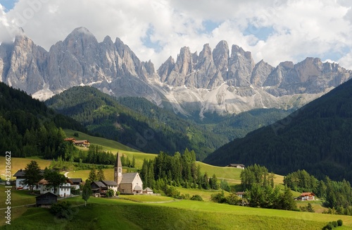 Idyllic scenery of Val di Funes in summer season with rugged peaks of Odle mountain range in background & a church in Village Santa Maddalena in the green grassy valley in Dolomiti, South Tyrol, Italy