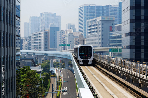 Scenic view of a train traveling on elevated rails of Yurikamome Line in Downtown Tokyo  with a background of modern buildings near Takeshiba Station under blue sunny sky   Scenery of a vibrant city