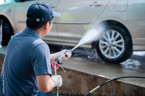 Asian man in uniform hands washes his car with a large head of water from a karcher and washing car with soap. Cleaning and disinfection. Car wash service concept.