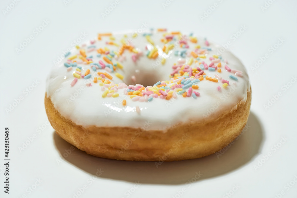 Junk food. Close up shot of a freshly baked delicious donut with colorful sprinkles and white sugar glaze isolated on light background Junk food. Close up shot of a freshly baked delicious donut with colorful sprinkles and white sugar glaze isolated on light background