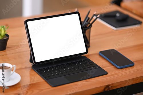 Close up view of digital tablet with wireless keyboard, coffee cup and smart phone on wooden table in meeting room.