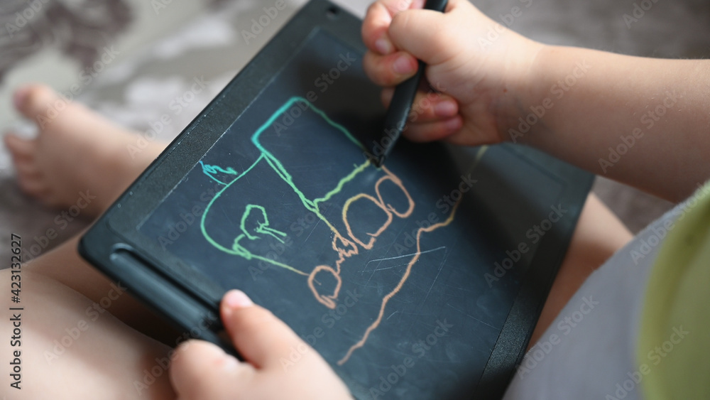 Close-up photo of a kid playing with drawing board on the sofa. Little child draws Close-up photo of a kid playing with drawing board on the sofa. Little child draws