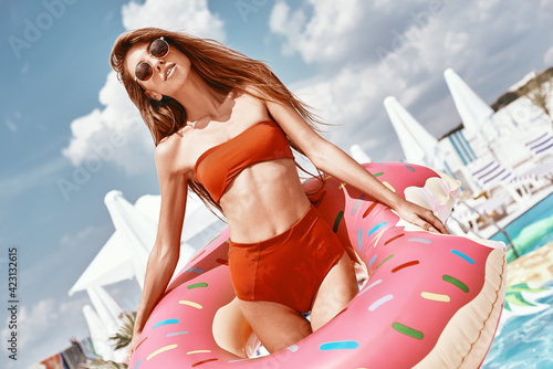 Beautiful one day, perfect the next. Sexy woman is wearing red bikini and holding inflatable swim ring in shape of donut