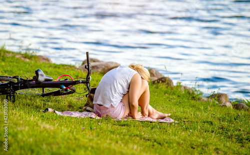 A girl with a bicycle sits on the shore of a lake © licvin