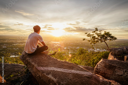 man sitting relax on top of a moutain watching the sunset