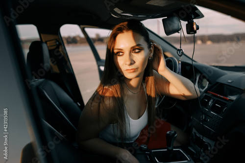 Beautiful young girl driving a car in the evening in the sunset sun on an empty parking lot