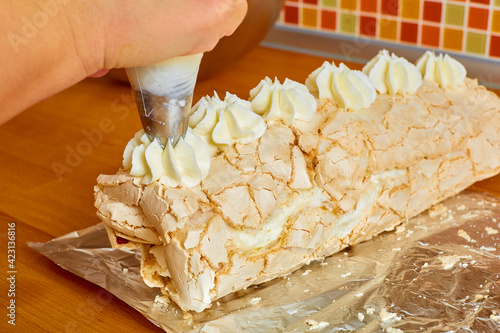 the sweet roll lies on the foil the cook's hand squeezes a white cream cream onto it from the cooking bag photo