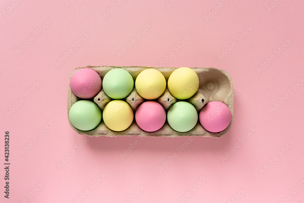 Easter eggs painted in pastel colors in cardboard box on pink background, top view - obrazy, fototapety, plakaty 