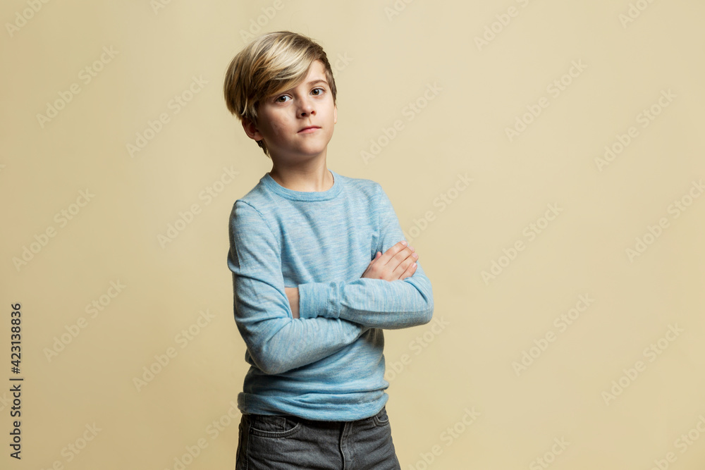 Serious boy with crossed arms. A guy of 9 years old with a fashionable hairstyle in a blue sweater. Yellow background. Serious boy with crossed arms. A guy of 9 years old with a fashionable hairstyle in a blue sweater. Yellow background.