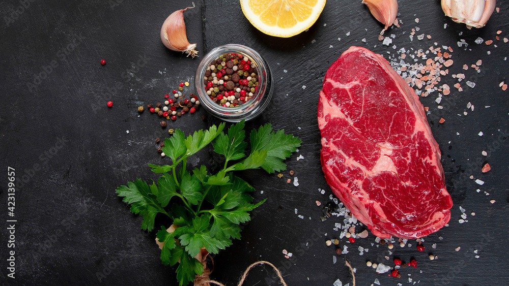 Meat raw steaks with seasoning and herbs on dark background.