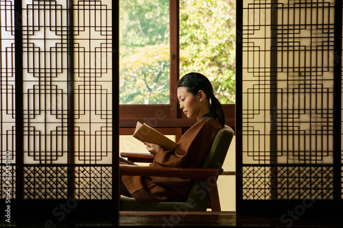 Serene young woman reading book behind patterned shoji doors
 photo