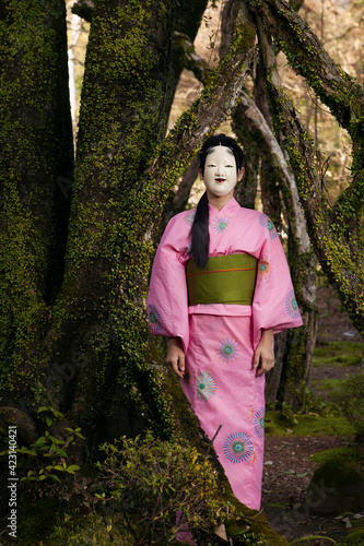 Portrait young woman in pink kimono in Japanese Noh mask at tree
 photo